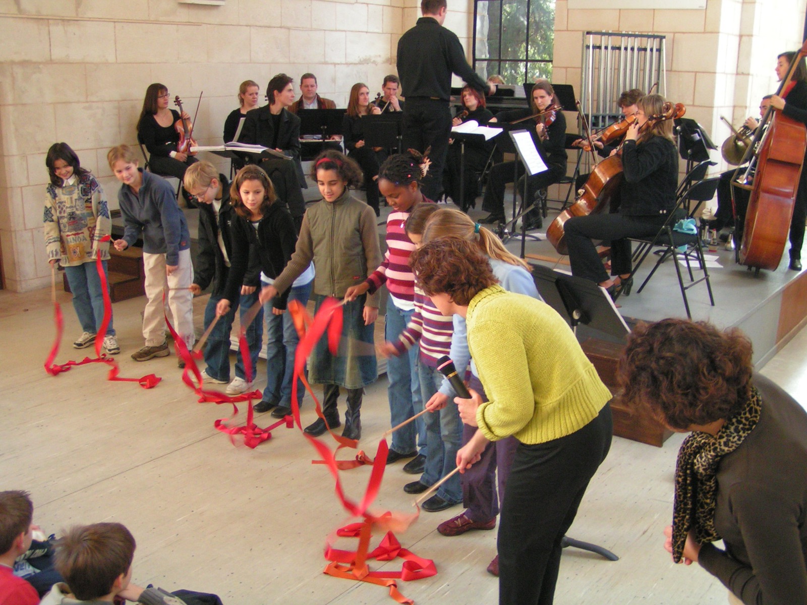 Des enfants dansent avec des rubans rouges devant un orchestre