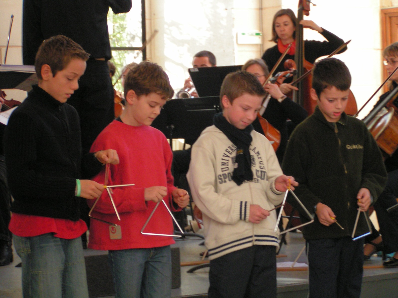 Des enfants jouent du triangle devant un orchestre