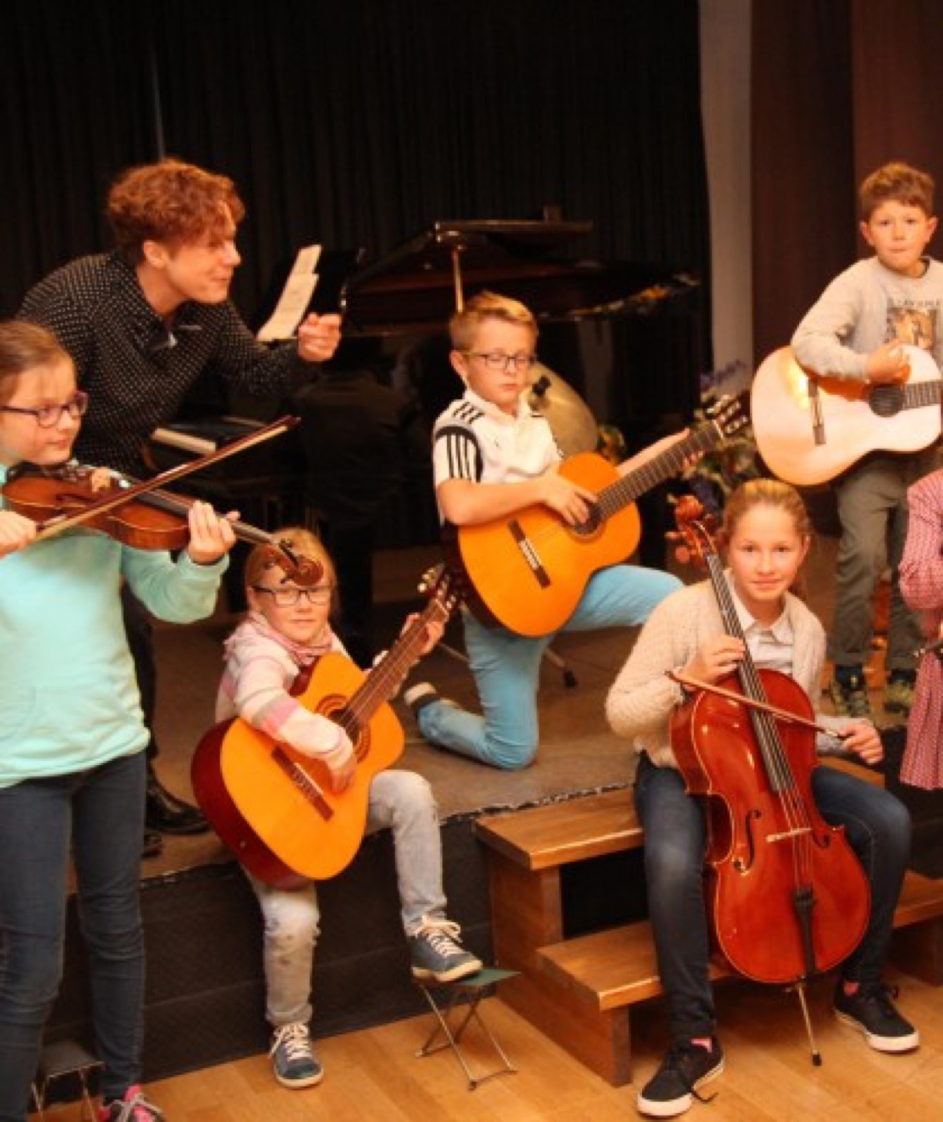 Des enfants jouent du violon, de la guitare et du violoncelle sur scène